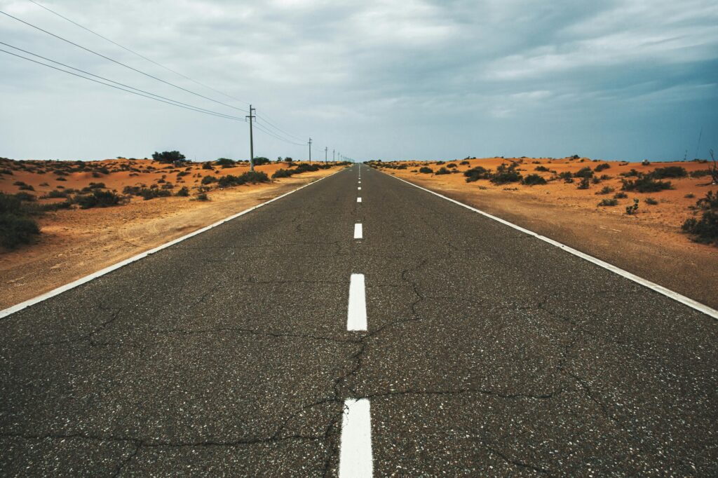 Straight, empty desert road under cloudy sky in Dubai, UAE, highlighting solitude and vastness.