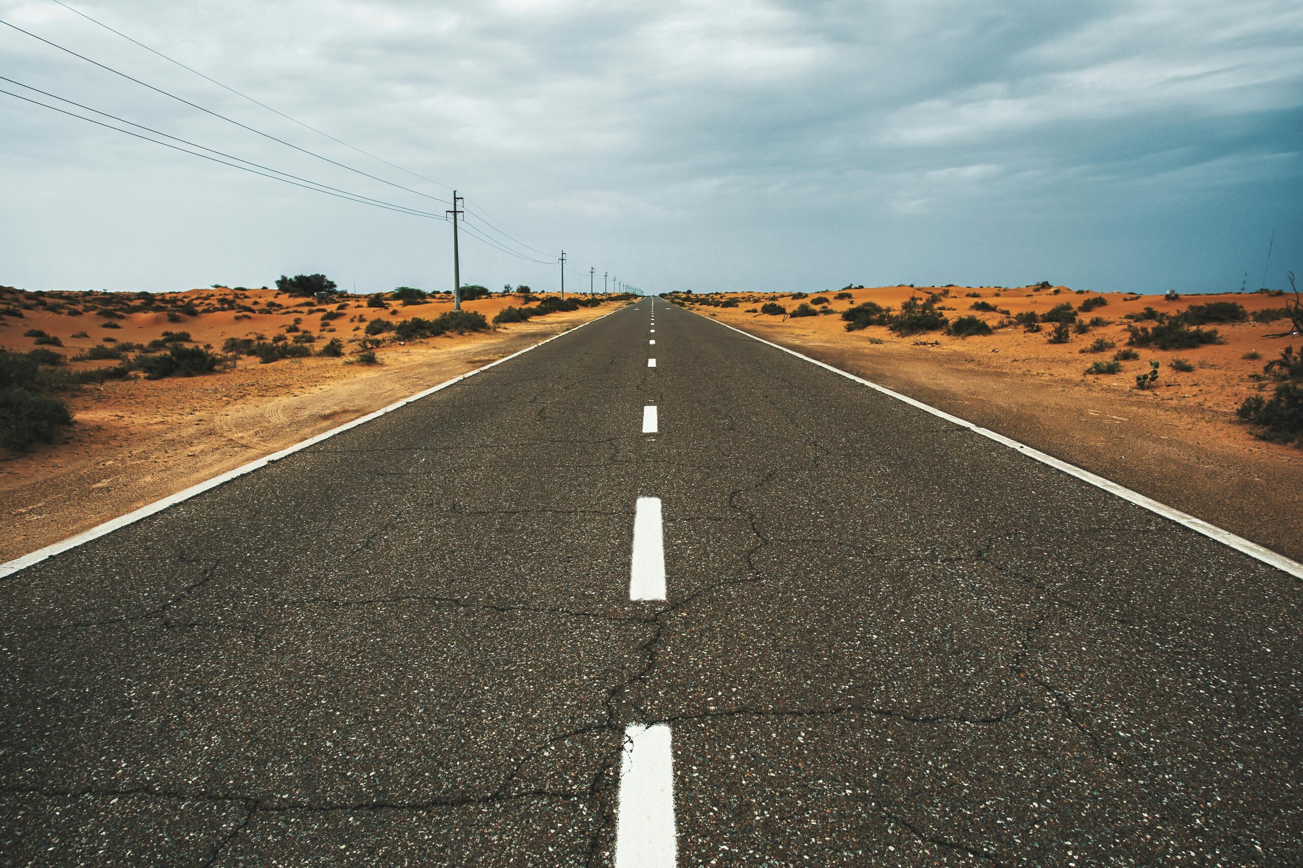 Straight, empty desert road under cloudy sky in Dubai, UAE, highlighting solitude and vastness.